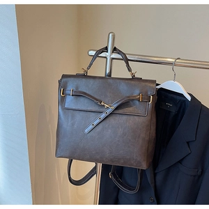 Detail of vintage dark gray leather backpack with brass hardware on an indoor clothes rack