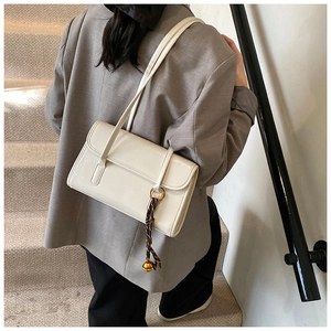 Detail of white glossy leather shoulder bag with decorative brown woven pendant charm