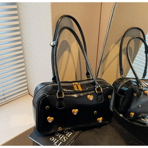 Close-up of black glossy underarm bag with gold heart-shaped studs and mirror-like texture