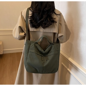 Detail view of olive green nylon tote bag with wide strap on a model's back