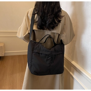 Detail of a large black nylon tote bag with dual zippers worn with a khaki trench coat
