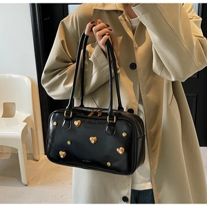 Detail of a vintage black Boston bag with gold heart studs held by a model in a trench coat