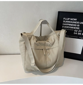 Detailed close-up of a large beige nylon tote bag with functional pockets on a white pedestal