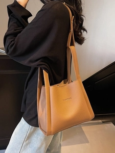 Minimalist tan pebbled leather bucket bag shown as a versatile shoulder tote with long strap