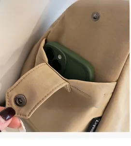 Detail of a khaki canvas bag side pocket with metal snap button holding a smartphone