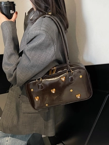 Deep brown glossy shoulder bag with heart rivets and gold hardware on model