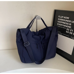 Detail of dark blue nylon tote bag showing front hidden zipper pockets and strap