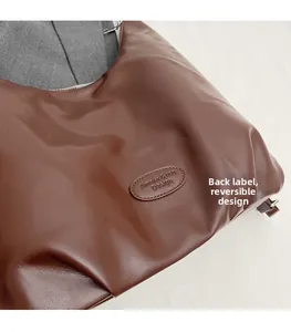 Detail view of brown leather tote bag with embossed oval label and textured finish