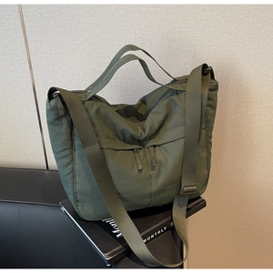 Detailed view of the olive green nylon tote bag featuring front zip pocket and dual straps