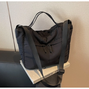 Detail of black nylon tote bag with vertical zip pockets resting on white books