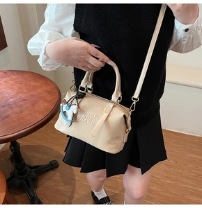 Detail of beige leather boston bag featuring letter embossing and a horse charm