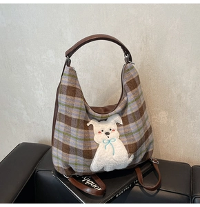Detail of plaid tote bag featuring fuzzy puppy patch and brown leather straps