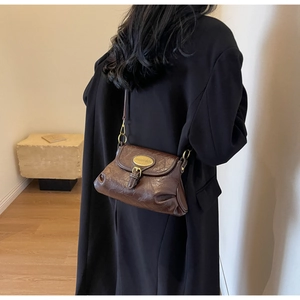 Detail of vintage dark brown oil wax leather bag with golden metallic oval logo buckle