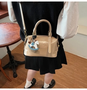 Close-up of beige faux leather Boston bag with embossed lettering and horse charm