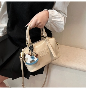 Detail of beige leather boston bag with embossed lettering and horse charm accessory
