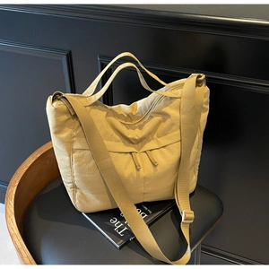 Detail of khaki nylon tote bag featuring front dual zipper pockets on a leather chair