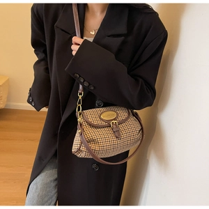 Detail of houndstooth crossbody bag with brown leather trim and golden metal emblem