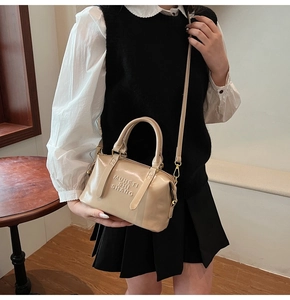 Beige patent leather handbag with embossed letters and adjustable shoulder strap on model