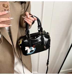 Detail of glossy black Boston bag featuring embossed letters and a blue rocking horse charm