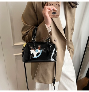 Detail of black glossy Boston bag with embossed letters and a horse charm on a model