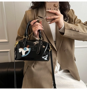 Close-up of black patent leather handbag with embossed letters and a rocking horse charm