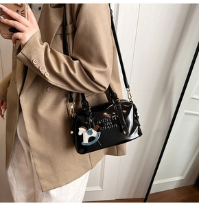 Detail of glossy black Boston bag with MUHSHI SHANG embossing and horse charm