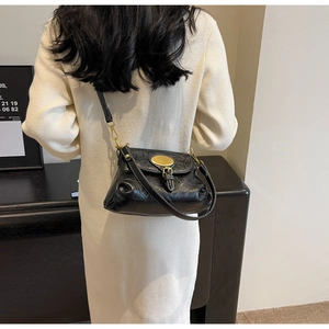 Detailed view of black textured leather crossbody bag with vintage gold metal buckle