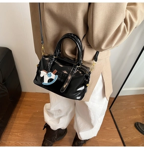 Detail of glossy black patent leather Boston bag with embossed letters and charm
