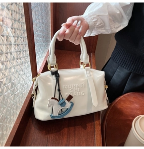Detailed view of white Boston bag featuring embossed letters and rocking horse pendant