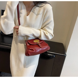 Detail of a vintage dark red leather crossbody bag with a gold oval metal clasp detail