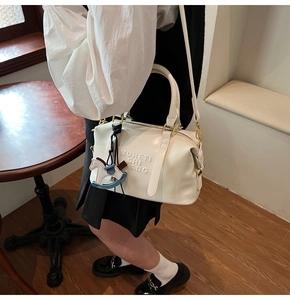 Detail view of white Boston bag with embossed text and decorative horse charm pendant
