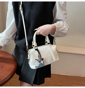 Close-up of white Boston bag featuring embossed logo and a decorative horse pendant