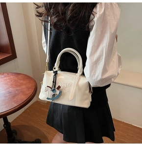 Detail view of white leather boston bag with MUHETI SHI FANG letters and horse charm