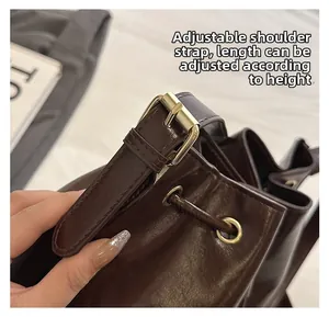 Détail de la bandoulière réglable avec boucle dorée sur le sac seau en cuir marron foncé