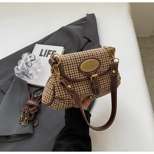 Detail of retro houndstooth pattern fabric and golden metal logo on brown leather bag