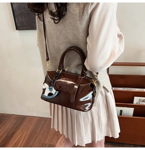 Brown glossy boston bag with letter embossing and horse charm worn by a model