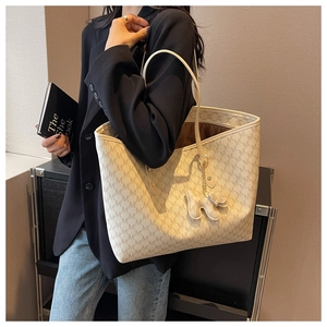 Close-up of cream tote bag with M-letter print and cute dog charm on a model's shoulder