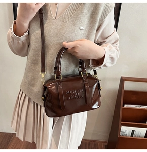 Detail of glossy brown handbag with embossed lettering and premium gold hardware