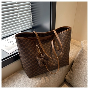 Close-up of caramel brown tote bag with M-pattern print and bear charm on sofa