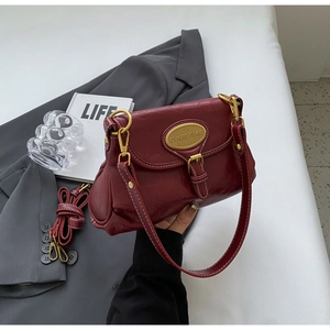 Detail of vintage burgundy leather shoulder bag with gold logo plate and pleated texture