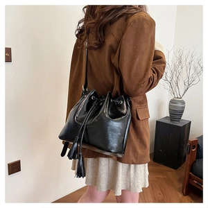Détail du sac seau noir brillant avec cordon de serrage, pompons et bandoulière fine
