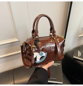 Detail view of glossy brown Boston bag with a blue horse charm and gold metal hardware