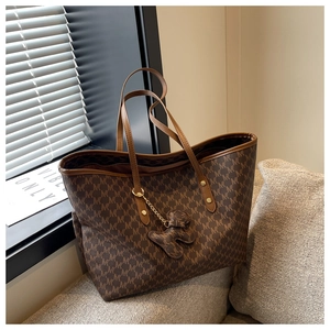 Detailed shot of brown monogram tote bag with cute bear charm on a soft gray sofa