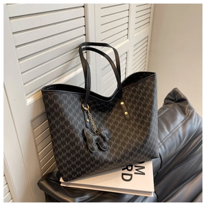 Detail of black tote bag with geometric M-pattern, leather handles and dog charm accessory