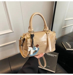 Detail of beige Boston bag with embossed lettering and a colorful rocking horse charm