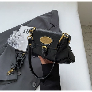 Detail of black glossy leather handbag featuring golden oval buckle and branded metal plaque