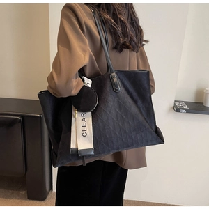 Detail of black quilted tote bag featuring a leather shoulder strap and decorative webbing