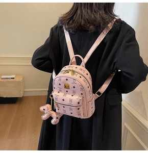 Detail view of a pink monogram mini backpack with gold logo plate and cute bear charm