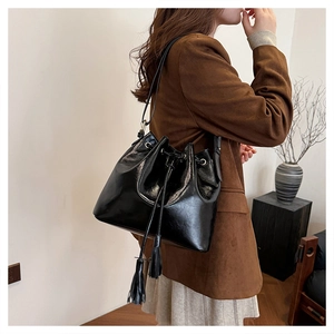 Détail d'un sac seau vintage en cuir noir avec cordon de serrage et pompons sur un modèle