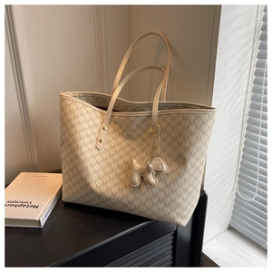 Detail of cream tote bag with M-pattern print, gold hardware and dog-shaped charm